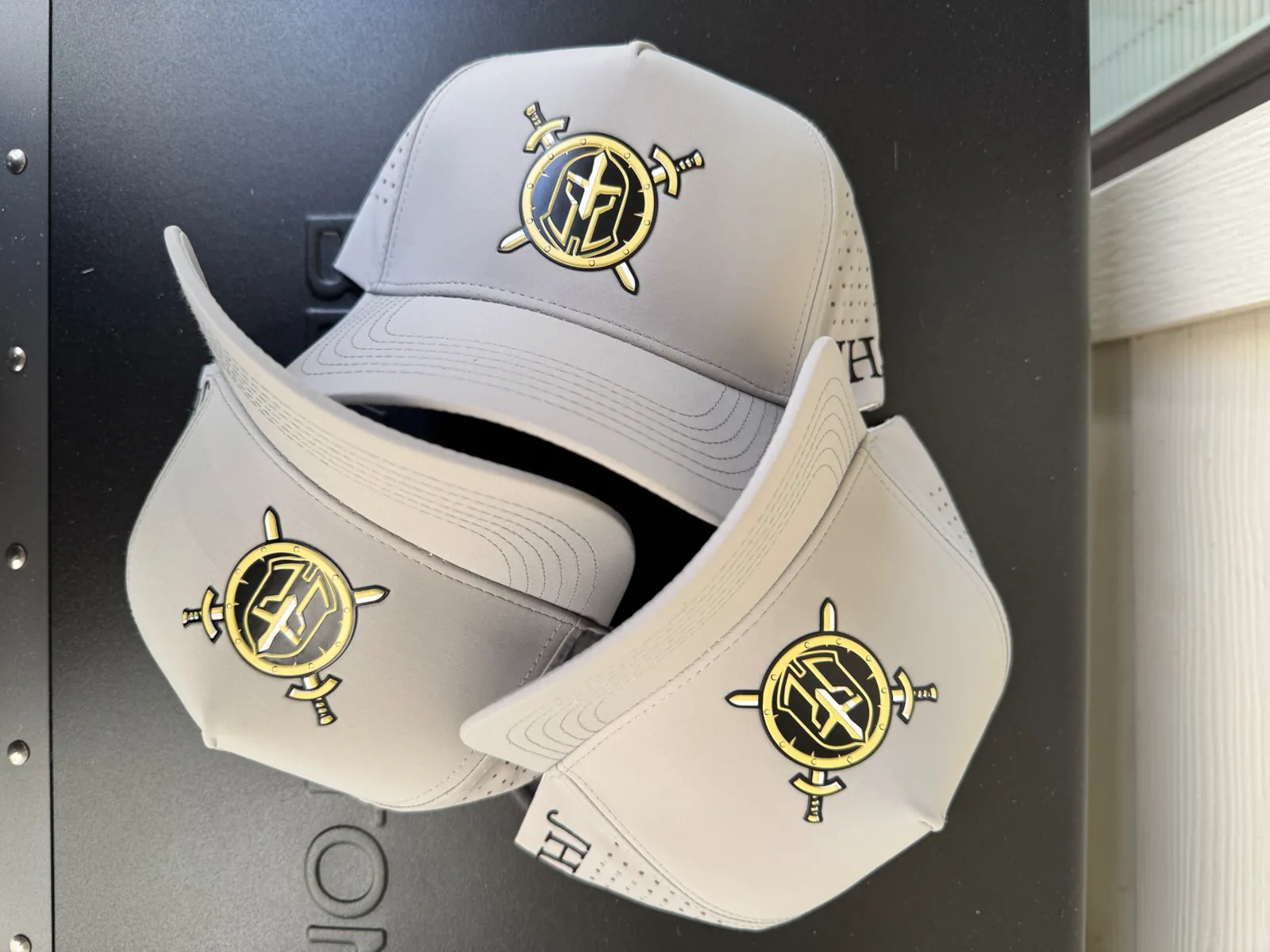Three gray performance hats with gold and black crest patches
