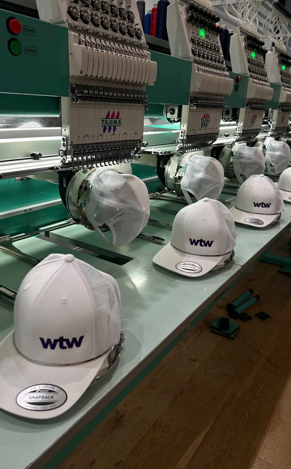 White corporate hats lined up across commercial embroidery machines