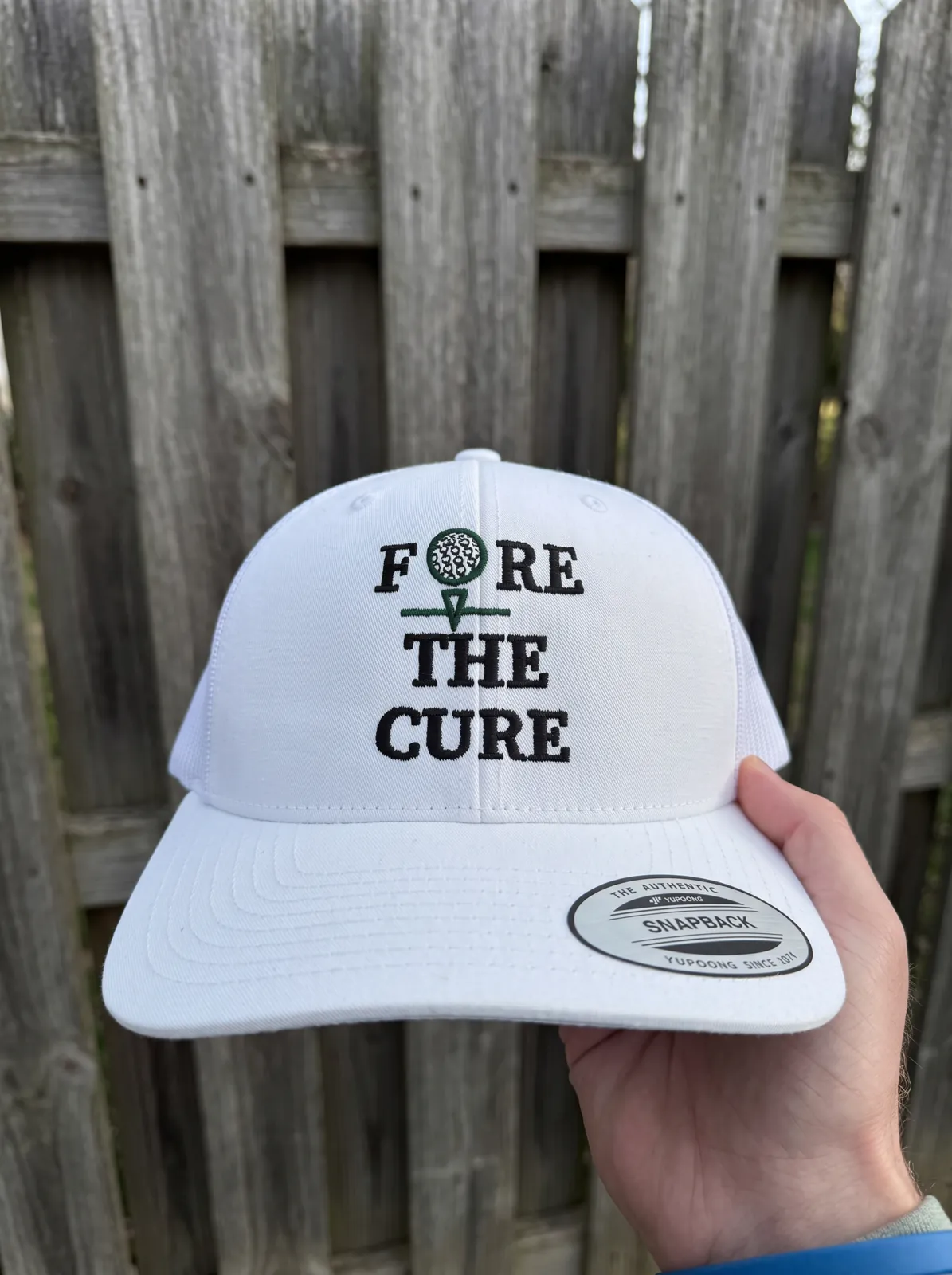 White trucker hat with black and green charity golf event embroidery