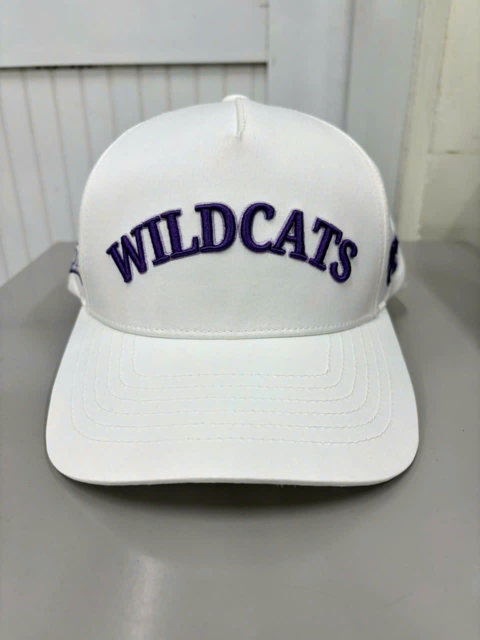 White hat with purple 3D puff team lettering across the front